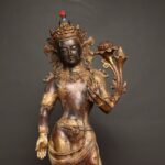 Antiqued bronze standing statue of Maitreya with left arm raised holding long unopened lotus stem